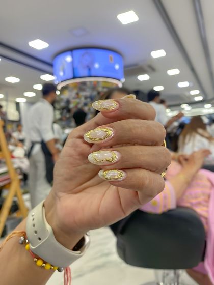 The final result of an airbrush and chrome nail set. This design features a white base with gold chrome swirls for an elegant and artistic look.