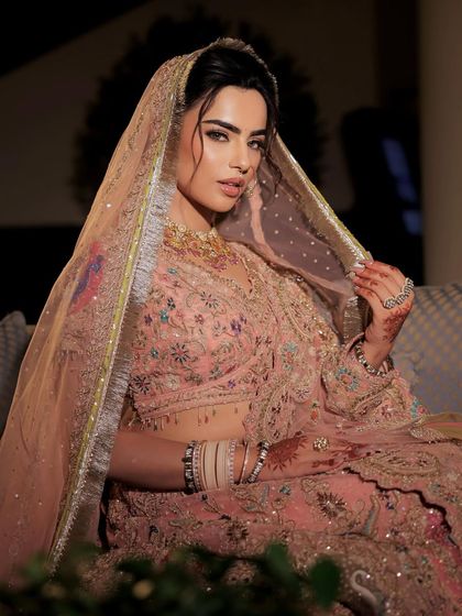 The bride under her veil, looking mysterious and elegant. The soft lighting highlights the shimmer in her makeup and the delicate embroidery of her outfit.