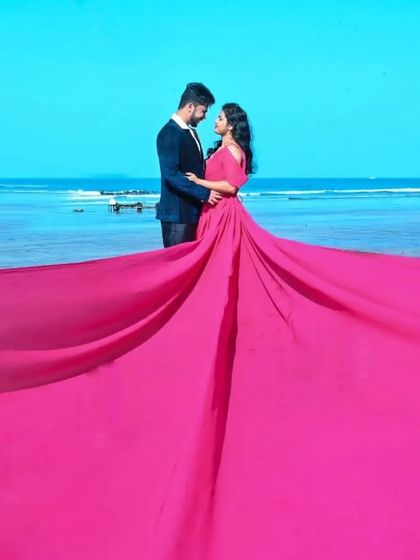 The entire frame is filled with the vibrant hot pink trail of the gown, creating a bold and abstract background for this romantic couple's portrait by the sea.
