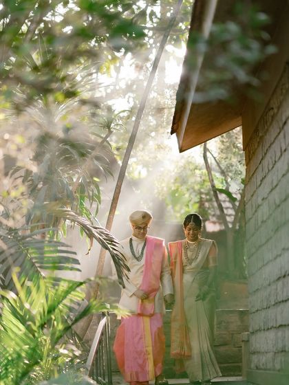 A couple is seen through a frame of lush palm leaves, with sunbeams breaking through, creating a dreamy and cinematic effect.