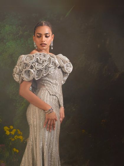 The silver Bellerose Gown, set against a mystical backdrop. The 3D cape and corset silhouette combine to create a look of pure enchantment.