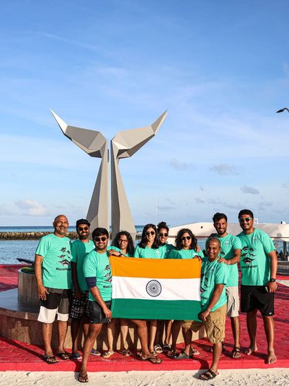Our dive team celebrating India's 75th Independence Day on land in the Maldives, standing proudly with the flag in front of a whale tail sculpture.