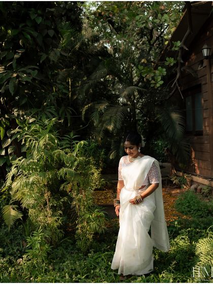 A beautiful black and white portrait of the bride in her white saree, walking through a lush garden. The natural setting and her graceful posture create a timeless image.