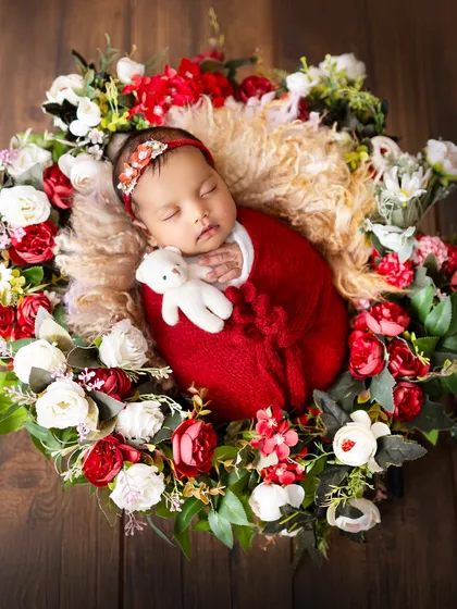 This sweet newborn is cuddled up with a tiny teddy bear, nestled in a bed of red and white flowers. Adding a small prop like a toy can add a touch of sweetness to the portrait.