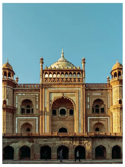 A frontal view of Safdarjung's Tomb, showing its grand scale and symmetrical design. The two small figures at the bottom provide a sense of the monument's immense size.