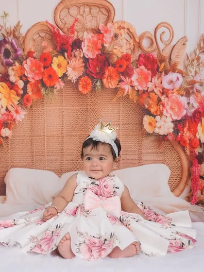 A happy smile from the birthday girl, seated on a miniature bed adorned with a beautiful floral headboard. This setup is perfect for a dreamy, whimsical theme.