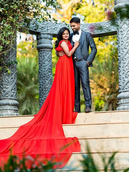 A romantic pre-wedding photo on a grand staircase, with the groom in a suit and the bride in a flowing red gown, capturing a classic, elegant moment.
