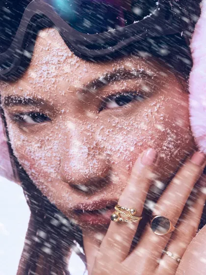 A close-up on the "frozen beauty" concept. The texture of the artificial snow on the skin, combined with the intense gaze, creates a compelling, high-fashion moment.