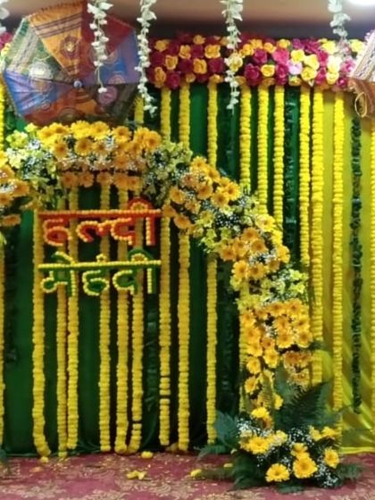 A combined "Haldi Mehandi" backdrop with a dense wall of marigold strings. The floral arch and hanging umbrellas add layers and texture to this traditional and colorful decoration.