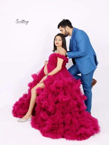 A romantic couple portrait with the husband kissing his wife's shoulder. The dramatic magenta gown and their elegant pose create a high-fashion, glamorous look.