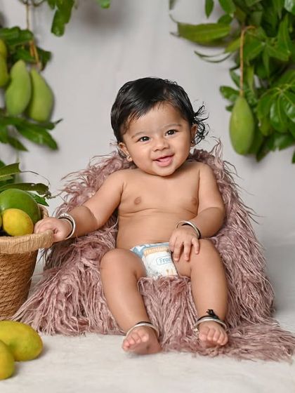 A happy baby sitting up in a chair made of fur, surrounded by mangoes.