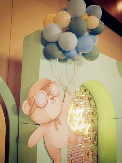 A cute pilot monkey prop holding balloons, with a 'Happy Birthday' neon sign glowing in the background.