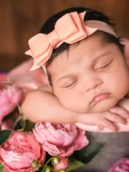 A beautiful newborn girl rests in a bucket surrounded by a bouquet of pink and purple flowers. A calendar block marks her birth date, making it a perfect birth announcement photo.