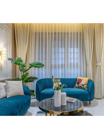 Sheer curtains diffuse the afternoon light, creating a soft glow in this modern living room. The crystal wall sconce adds a touch of glamour, blending seamlessly with the classic wall panels.