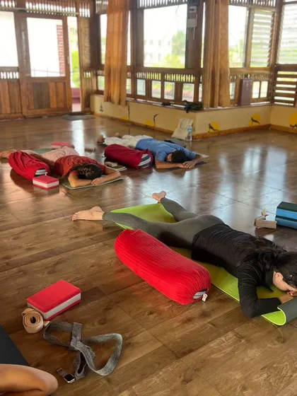 A wide shot of a Yin class, with students in various states of surrender, supported by an array of props like bolsters and blocks.
