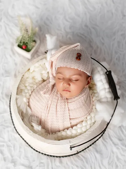 A classic newborn pose in a white bucket lined with soft, fluffy fabric. The baby is swaddled in a neutral color, creating a timeless and elegant portrait.