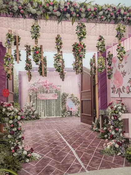 A stunning floral entrance to a wedding venue. The entire walkway is covered in intricate arrangements of purple and pink flowers, creating a luxurious and immersive experience.