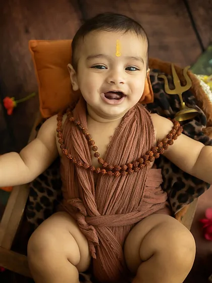 A baby dressed in honor of Lord Shiva, offering a beautiful, happy smile.