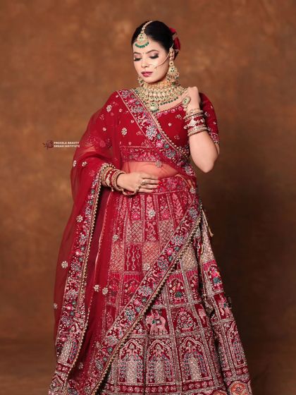 A full length shot of a bride in a deep red lehenga. The hair is styled in a classic bun with a flower, creating a traditional and elegant silhouette.