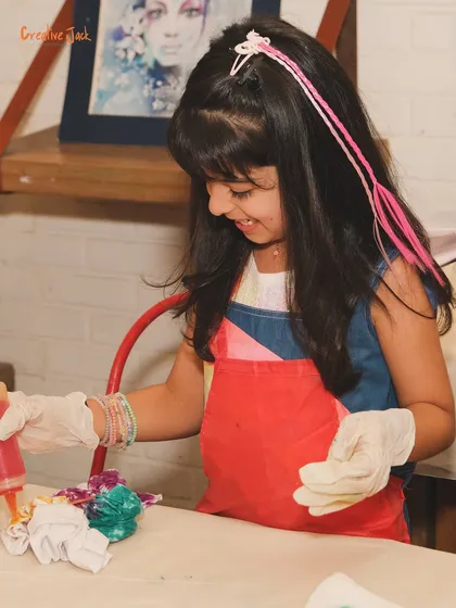 A young girl smiles as she carefully applies dye to a t-shirt. Tie-dye workshops are a favorite at birthday parties, offering a fun, hands-on experience.
