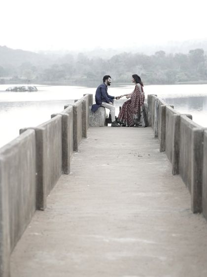 A quiet, reflective moment of a couple sitting on a concrete pier, dressed in traditional attire, looking out over the water.