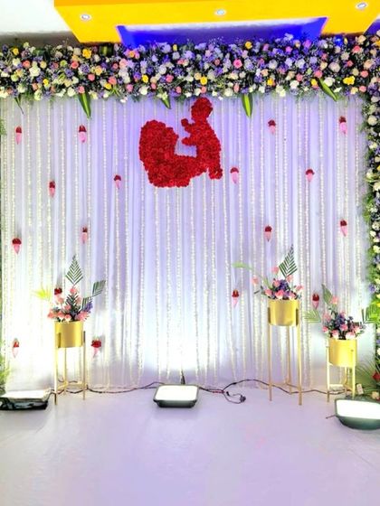 A beautiful Seemantham stage decoration with a white curtain and floral frame. The red flower silhouette of a mother and child is a lovely centerpiece.