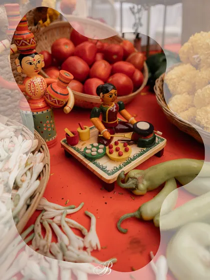 A close-up of a Channapatna toy depicting a woman cooking, set amongst fresh vegetables on the spice cart. This playful detail adds a narrative element to the decor, celebrating the theme of local life.