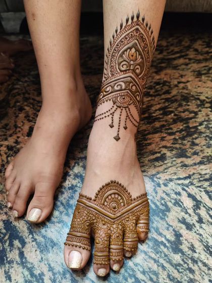 A side view of a minimalist bridal leg design. The pattern extends up the ankle like a piece of jewelry, with delicate hanging chains and a central lotus motif.