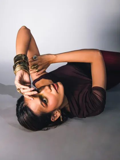 An unconventional pose that creates a unique and artistic composition. The model is lying down, looking up at the camera, which creates a disorienting yet captivating image. The lighting highlights the metallic sheen of the accessories and the creative makeup.