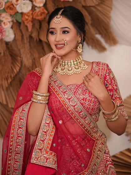 A happy model in a red and pink lehenga, showcasing a gold-toned Kundan choker and matching bangles.