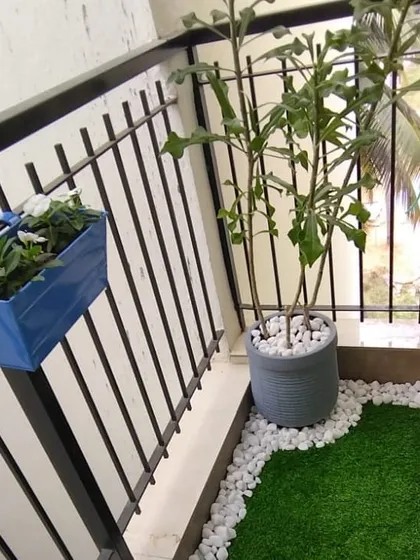 This image shows how we combine different elements like a blue railing planter, a larger floor planter, and an artificial grass patch with a pebble border to create a clean and modern balcony garden.