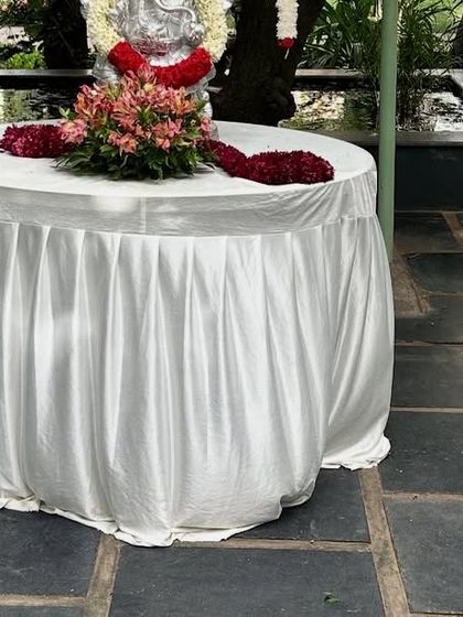 We provide various types of tables for different event needs. This round table is covered with a white satin skirt, perfect for placing a cake, gifts, or a religious idol.