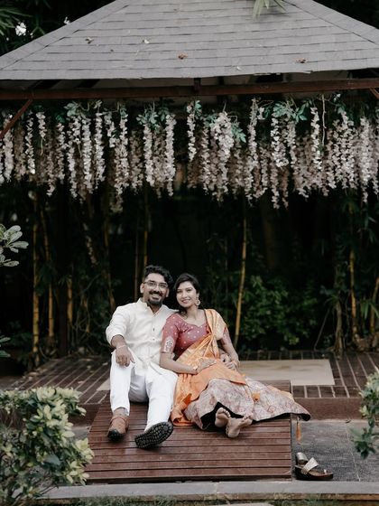 A smiling portrait of a couple sitting under a flower-adorned gazebo, capturing a moment of shared joy.