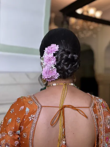 A detailed shot of a braided bun decorated with a line of fresh purple flowers. The intricate braiding adds texture and dimension, making it more than just a simple floral bun.