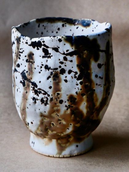 A handmade cup with a dramatic splash of black and brown glaze over a white base. The energy of the splash makes each cup feel alive and full of movement.