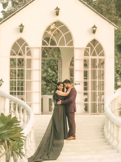 A fairytale moment from a pre-wedding shoot, featuring the couple in front of a beautiful white chapel-like structure. The bride's flowing gown adds a touch of elegance to this romantic portrait.