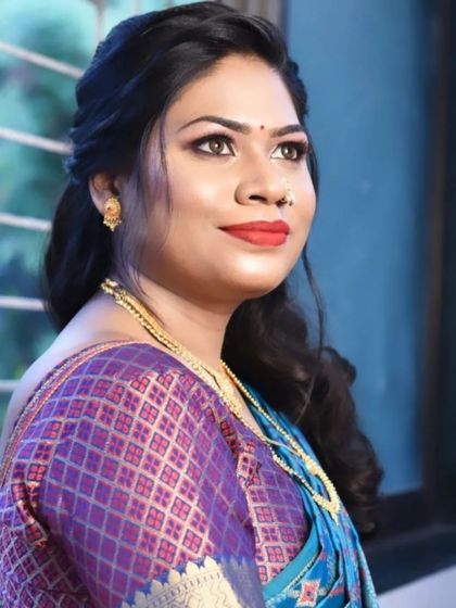 A posed shot of the bride from the previous video. Her makeup features a soft smokey eye and a bold red lip that stands out against her blue silk saree.