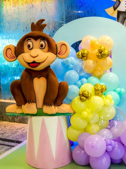 A cheerful monkey prop sitting on a circus pedestal, surrounded by pastel balloons.