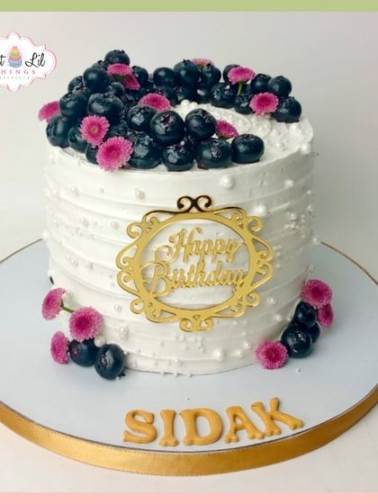An elegant birthday cake for Sidak, topped with a bounty of fresh blueberries and delicate pink flowers.