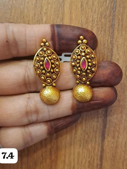 These oval antique gold-plated earrings feature a central stone and a textured golden ball drop. They are a beautiful and timeless design.