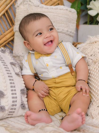 A happy baby boy in a yellow outfit that perfectly complements the warm tones of the boho setup. His smile lights up the entire frame.