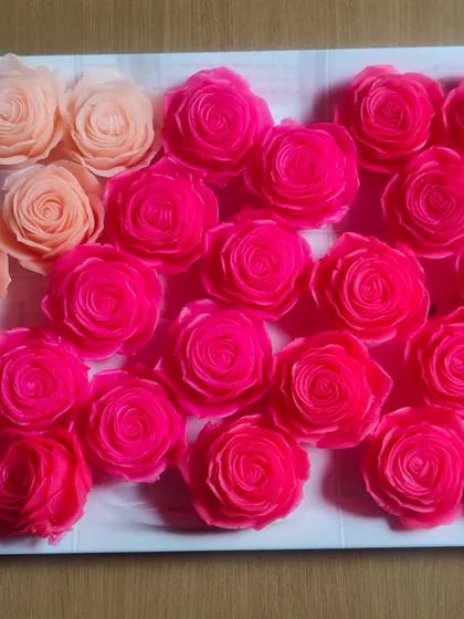 A tray of bright pink and peach rose-shaped soaps, ready for packaging.