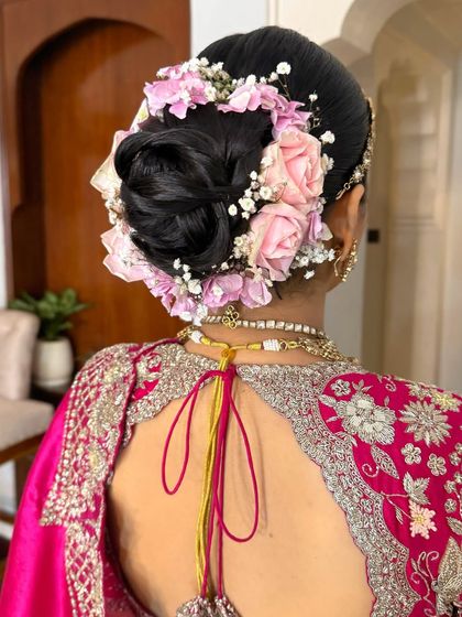 A back view of a low bridal bun, beautifully decorated with fresh pink roses and baby's breath for a soft, romantic feel.