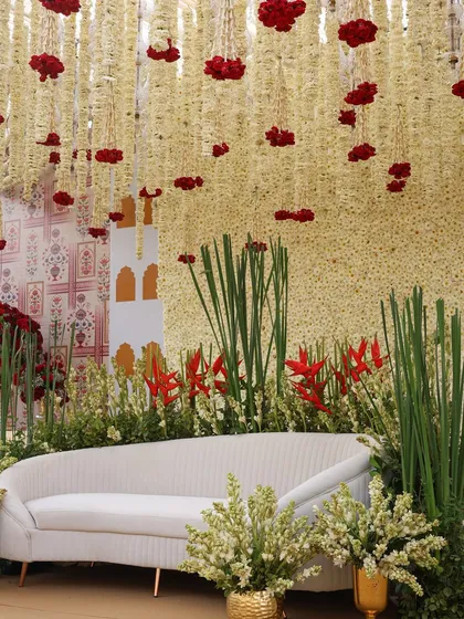 A modern take on traditional decor. This seating area features a backdrop of white flowers with pops of red, under a ceiling of hanging rajnigandha.