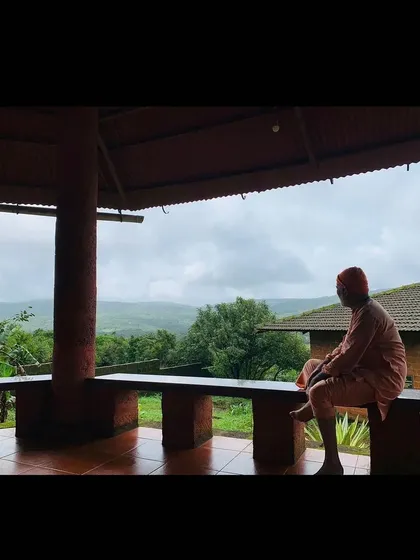 A moment of quiet contemplation on the ashram veranda. The monsoon clouds over the hills create a serene and introspective atmosphere.