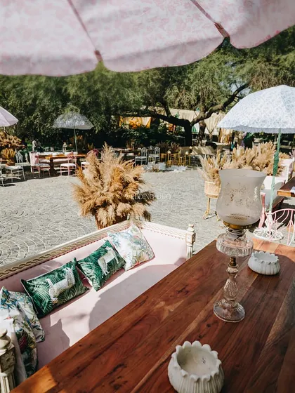 A chic lounge area for an eco-friendly wedding. We used a mix of wooden furniture, pampas grass arrangements, and printed parasols to create a relaxed and stylish space for guests.