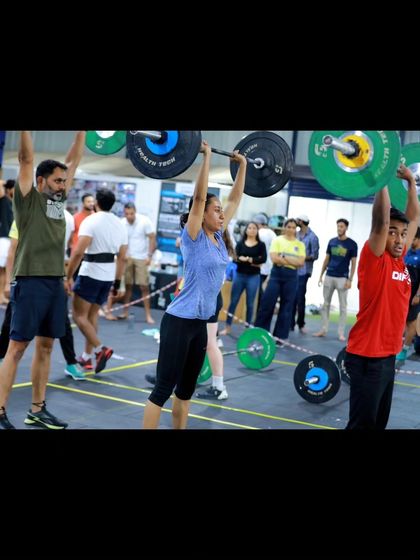 A female athlete successfully completes a heavy push jerk during a competition, with teammates and spectators cheering her on. The energy at these events is a huge motivator.
