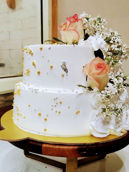Simple, elegant, and beautiful. This two-tier white cake is decorated with fresh roses, baby's breath, and a sprinkle of gold and silver edible beads, perfect for an intimate wedding or engagement.