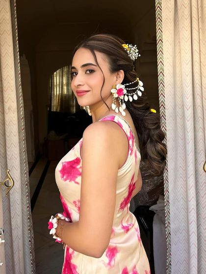 The client turns to show the side profile with her floral braid. The hairstyle is complemented by matching floral jewelry, creating a cohesive and stunning look.