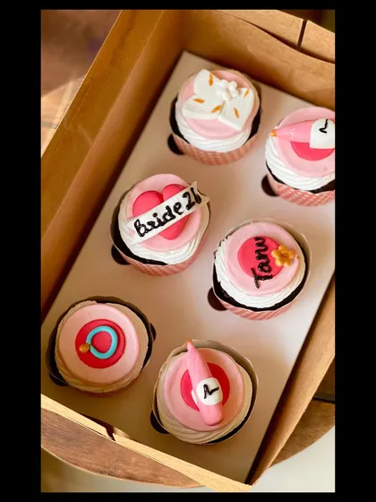 A fun and girly set of "bride to be" cupcakes. These pink cupcakes feature fondant toppers like a champagne bottle, a ring, and a banner.